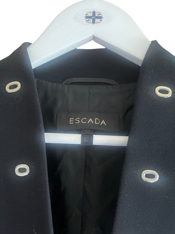 A close-up of a black Escada coat hanging on a white hanger, showing the brand label and silver-tone grommet details.