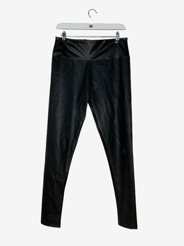 Black faux-leather leggings hanging from a white plastic hanger against a light gray background.