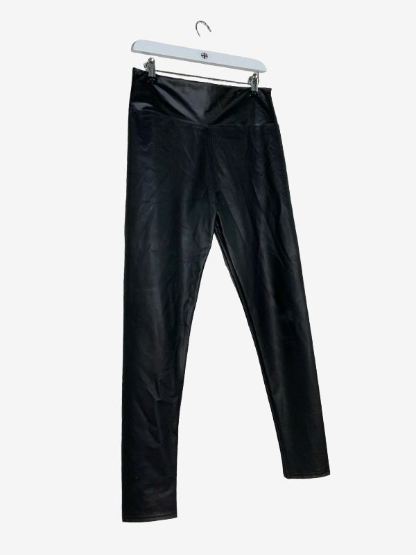 Black faux-leather leggings hanging from a white plastic hanger against a light gray background.