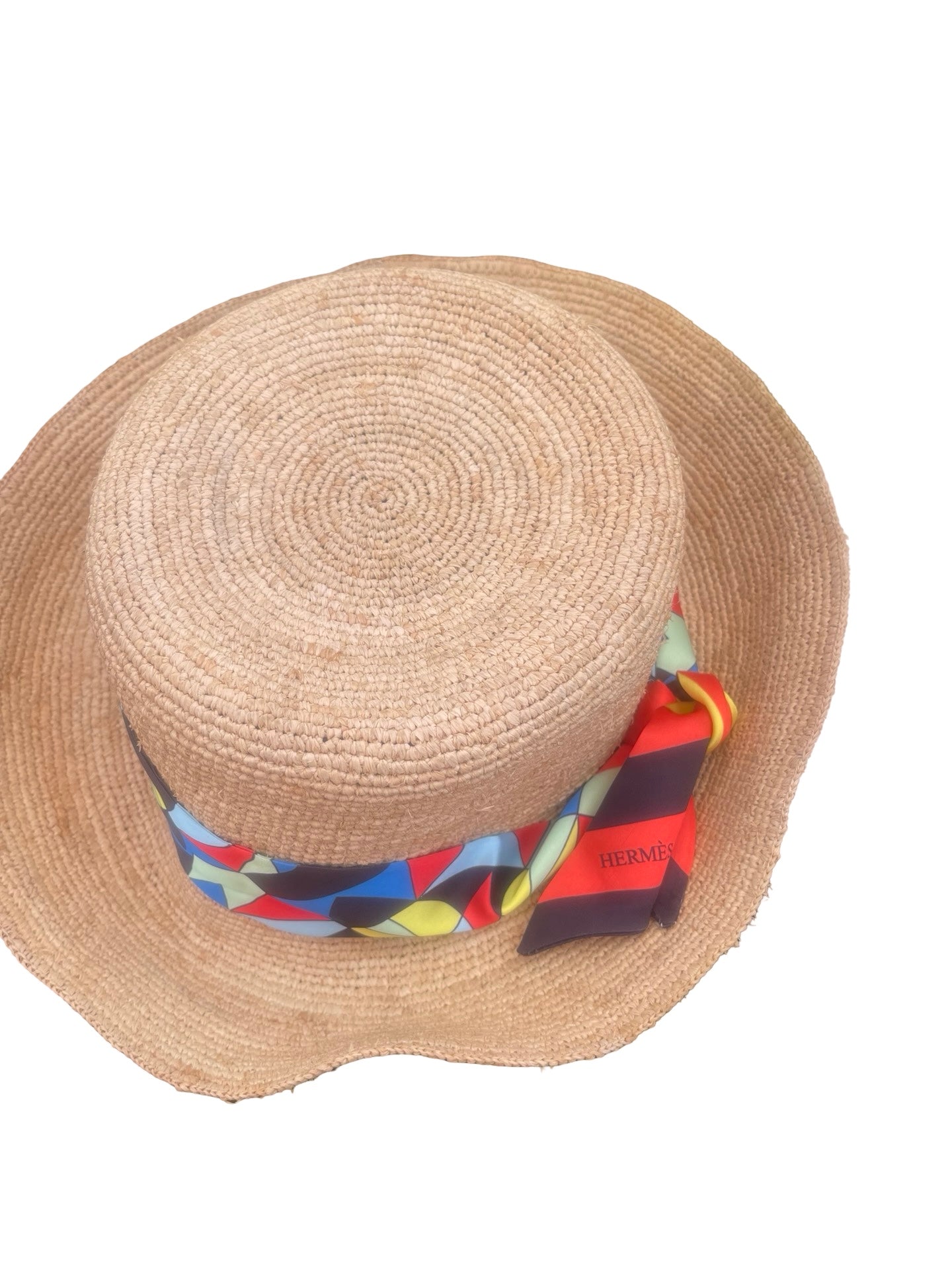 A natural straw boater hat with a colorful geometric patterned silk band tied around the crown, shown on a plain white background.