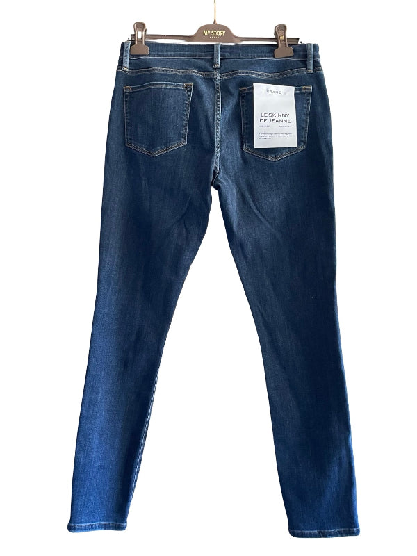 Back view of dark blue skinny jeans hanging on a wooden hanger against a white background, showing the back pockets and a white paper tag.