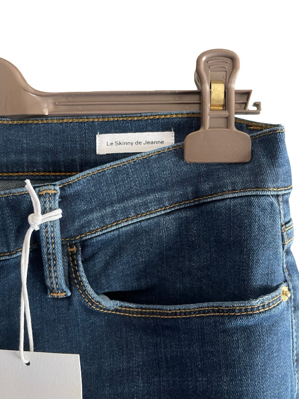 Close-up of a pair of blue denim jeans hanging from a gray plastic hanger with a white drawstring and a visible waistband label reading 'Le Skinny de Jeanine'.