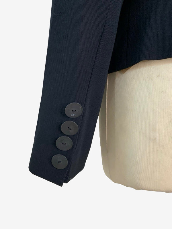 Close-up of a black blazer sleeve with four dark buttons, displayed on a cream-colored mannequin against a white background.