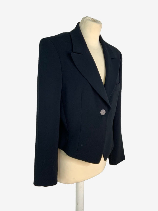 A black cropped blazer with a single button closure, displayed on a cream-colored mannequin torso against a plain white background.