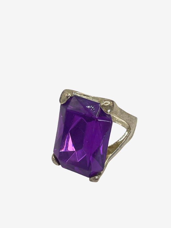 A silver ring featuring a large, faceted purple rectangular gemstone, set against a plain light gray background.