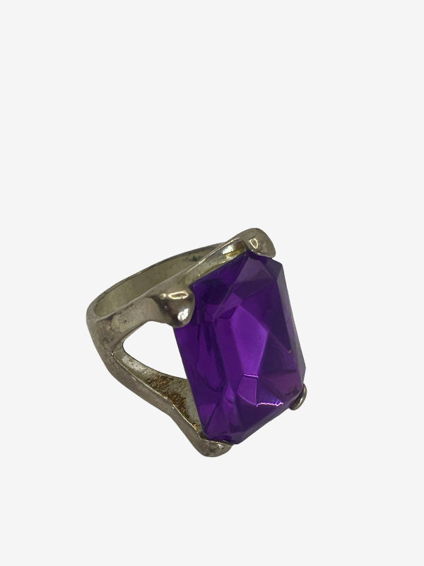 A silver-toned ring featuring a large, faceted purple gemstone, shown against a plain light gray background.