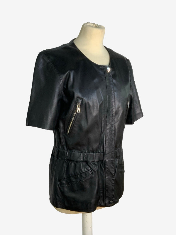 A black lambskin leather short-sleeve jacket with a zippered front and side pockets, displayed on a cream mannequin torso against a light gray background.