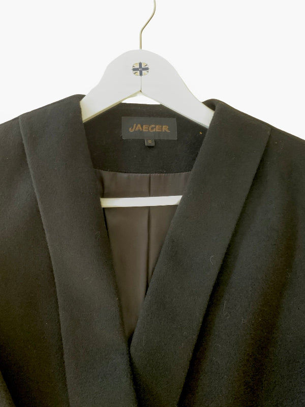 A black Jaeger coat with wide lapels hanging on a white wooden hanger against a plain white background.