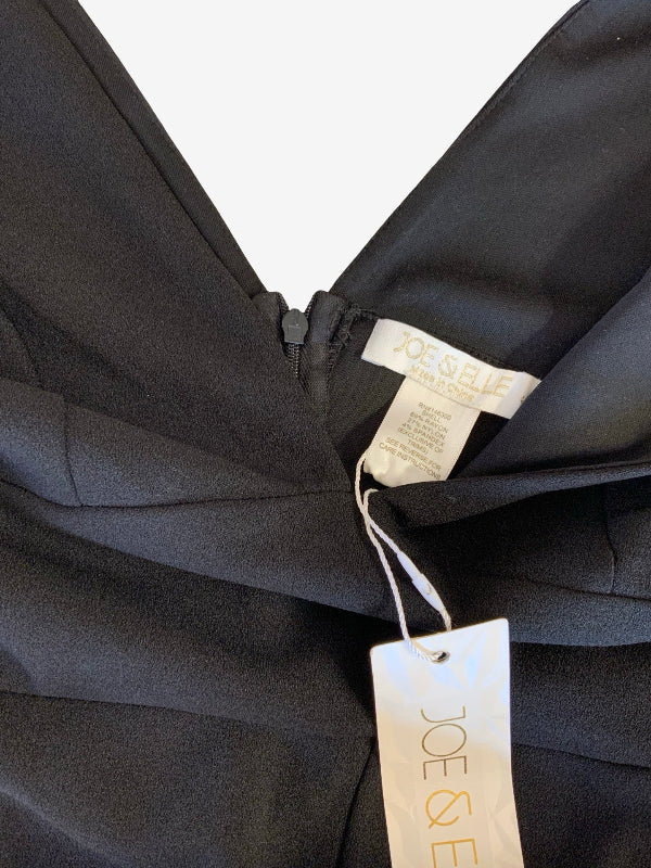Close-up of a black garment with a visible interior neckline, zipper, and two tags reading JOE & Elle on a white background.