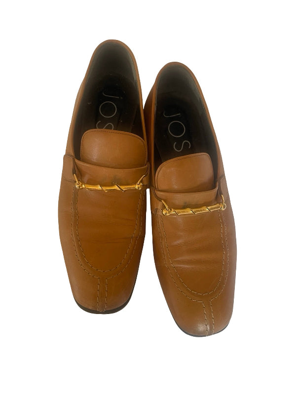 A pair of tan leather loafers with a gold-tone chain detail across the vamp, shown from a top-down view on a white background. The brand name 'jos' is visible on the inner sole of the left shoe.