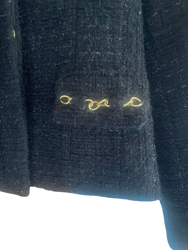 Close-up of a dark textured tweed jacket with a pocket featuring three gold-tone decorative loops on the front.