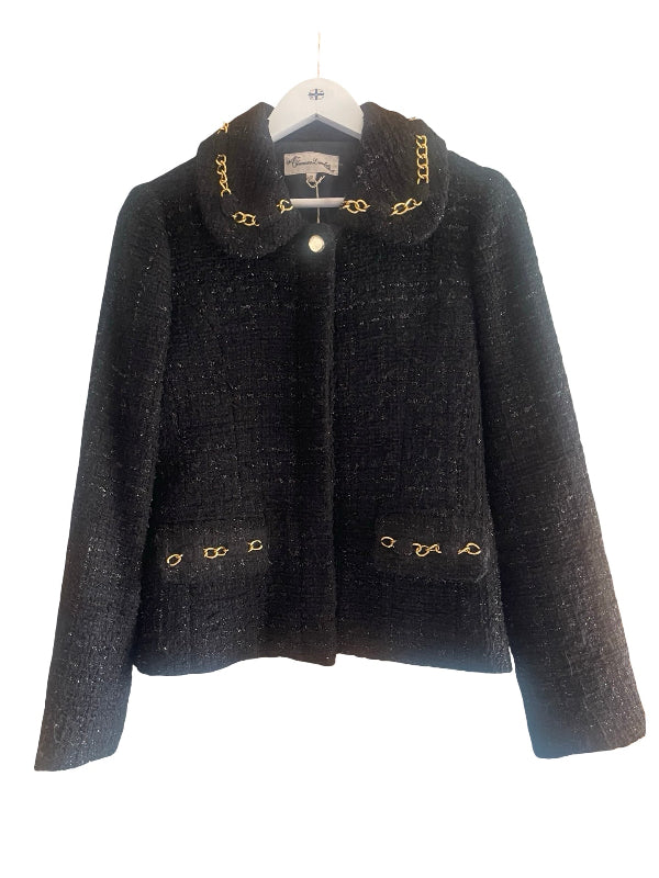 A black tweed jacket with gold chain accents on the collar and pockets, hanging on a white hanger against a white background.
