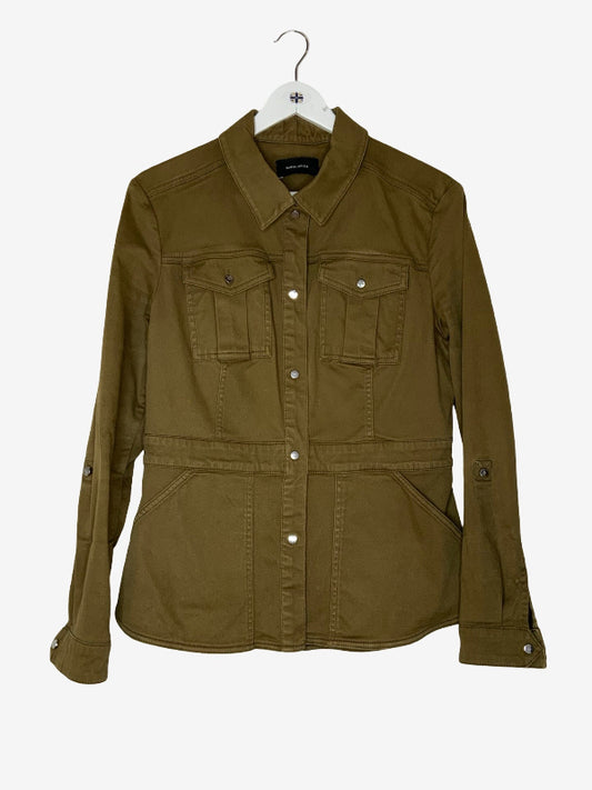 An olive green utility jacket with a pointed collar, button-up front, and four front pockets, hanging on a white hanger against a light gray background.