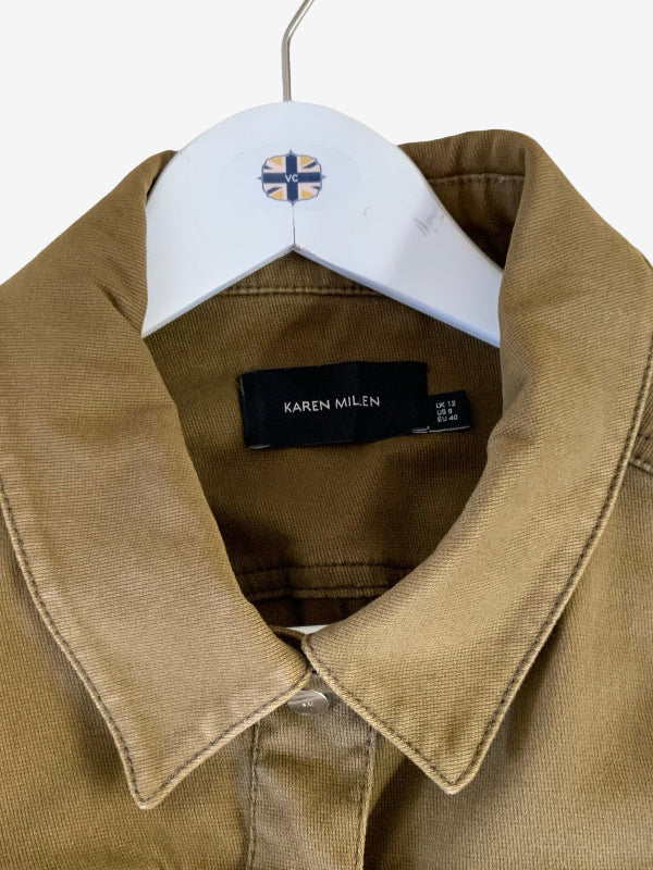 A close-up of a Karen Milen button-up jacket in a warm khaki color, hanging on a white hanger with the brand label visible inside the collar.