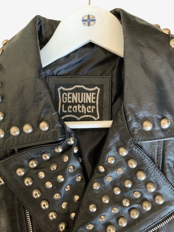 Black leather jacket with silver-tone studs, hanging on a white hanger with a 'Genuine Leather' brand patch visible inside the collar.