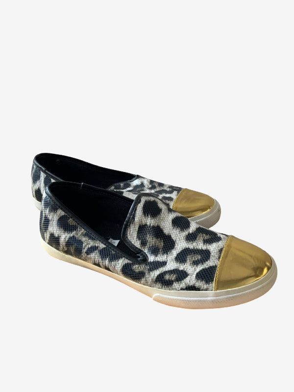 A pair of slip-on canvas sneakers featuring a black and white leopard print pattern, metallic gold toe caps, and beige rubber soles, shown on a light gray background.