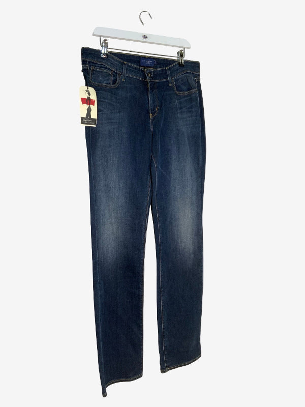 A pair of dark blue denim jeans hanging on a white plastic hanger against a light gray background, with a brand tag attached to the left side.