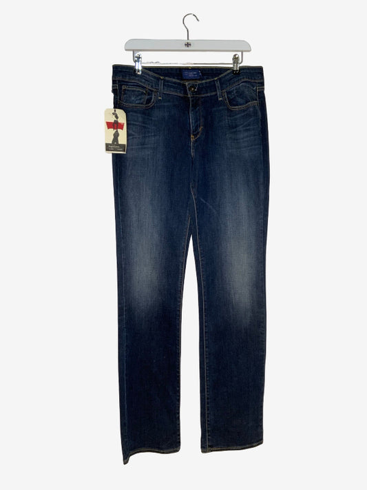 A pair of dark blue denim jeans with light wash fading on the thighs, hanging on a white plastic hanger against a light gray background.