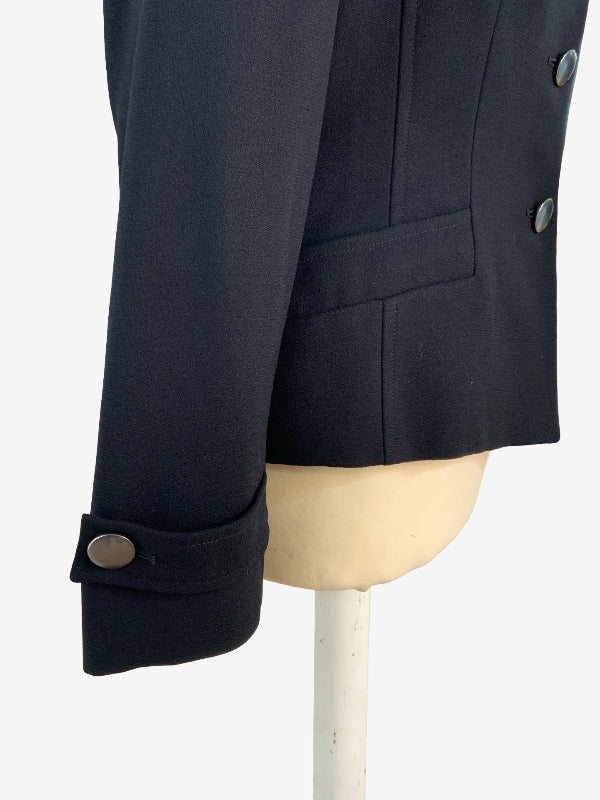 Close-up of a black tailored jacket displayed on a cream mannequin torso, showing a cuff with a single metal button and part of the front buttons 