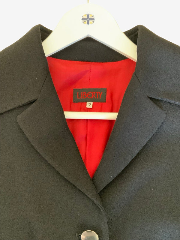 A close-up of a black jacket on a white hanger, showing a bright red inner lining and a black neck label that reads 'LIBERTY'.