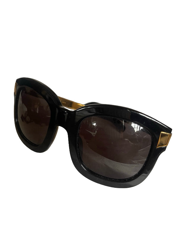 Oversized sunglasses with a glossy black acetate frame, dark brown tinted lenses, and gold metal accents on the temples, shown on a plain white background.