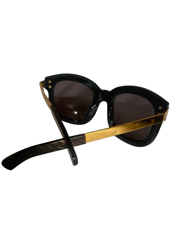 Black cat-eye sunglasses with dark lenses and gold metal temples, shown on a plain white background.