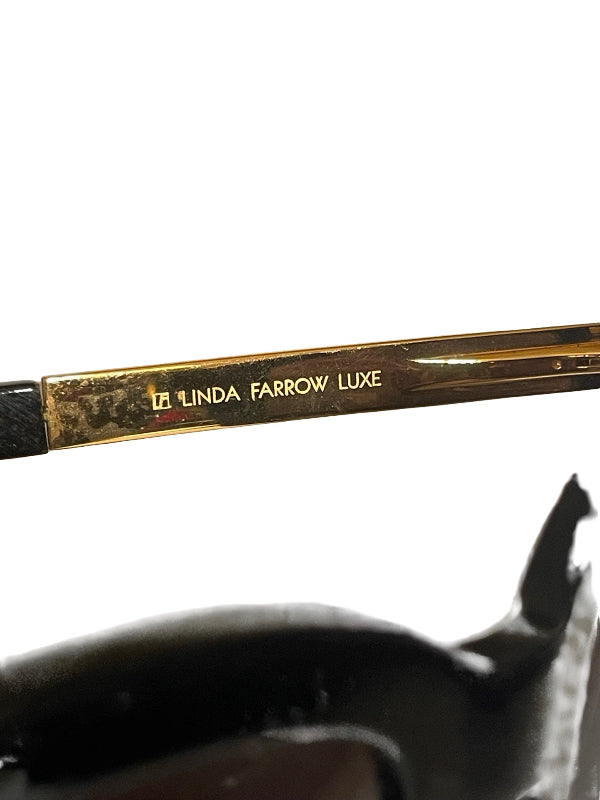 Close-up of a gold metal temple arm engraved with 'LINDA FARROW LUXE' on a white background.