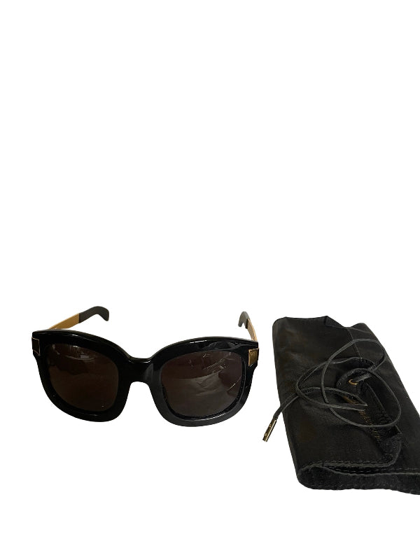 Black cat-eye sunglasses with dark lenses and gold-tone temple tips, shown next to a black fabric dust bag on a white background.