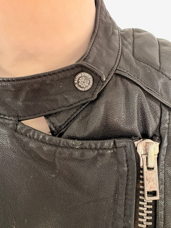 Close-up of a black leather jacket featuring a silver-tone snap button and zipper on a mannequin or model's neck.