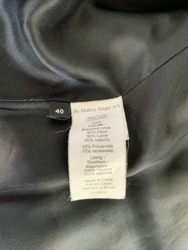 Close-up of a garment's interior label reading 'By Malene Birger' and size '40', attached to a dark charcoal gray fabric.