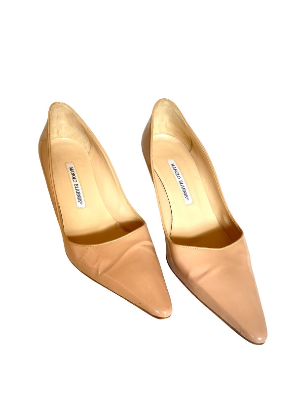 A pair of pointed-toe pumps in a light beige/nude color, shown from a top-down angle on a white background. The insoles display the ‘Manolo Blahnik”' brand label.