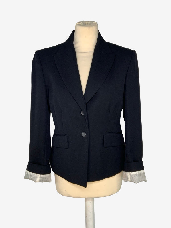 A black  tailored blazer jacket displayed on a cream-colored mannequin torso. The blazer features notched lapels, a two-button front closure, flap pockets, and contrasting light gray cuffs.