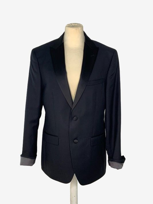 A men's black blazer with black satin peak lapels, displayed on a cream-colored mannequin torso against a light gray background.
