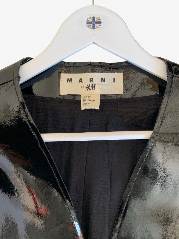 A close-up of a Marni by H&M garment hanging on a white hanger. The product has a glossy black patent-like exterior with a dark navy or black interior lining, and a visible MARNI by H&M neck label.