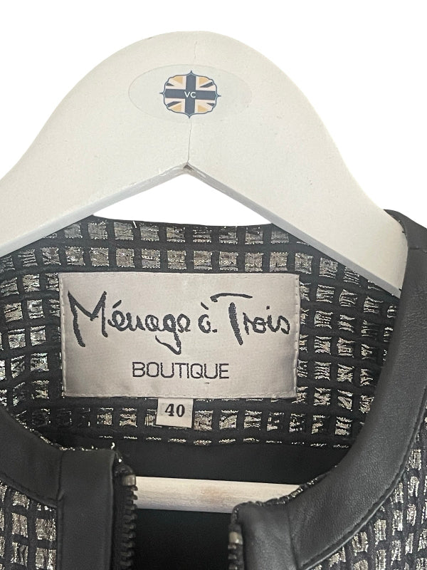 Close-up of the inside collar of a black and silver patterned jacket on a white hanger, showing the brand label 'Ménage à Trois BOUTIQUE' and size 40.