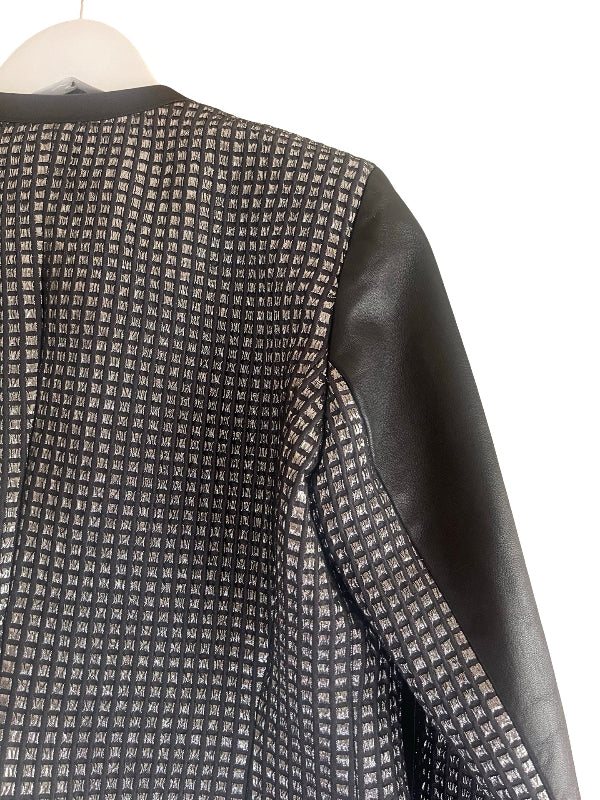 Close-up of a black and white patterned jacket with solid black leather sleeves, shown on a hanger against a white background.