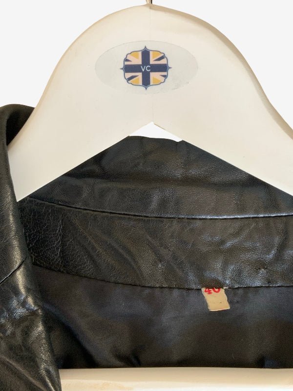 A close-up of a black leather jacket hanging on a white wooden hanger. The hanger features a circular logo with the letters 'VC' in a blue and yellow cross design.