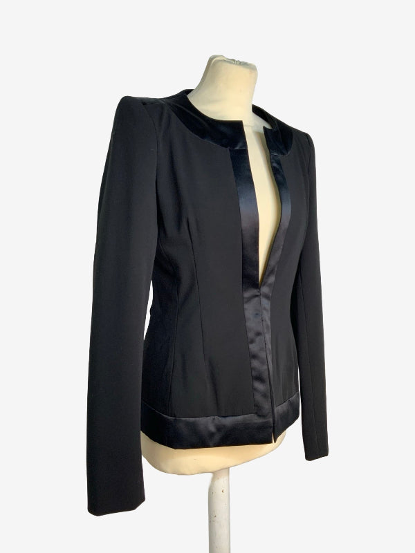 A black long-sleeve jacket with a satin-trimmed collar and front opening, displayed on a cream mannequin torso against a plain light background.