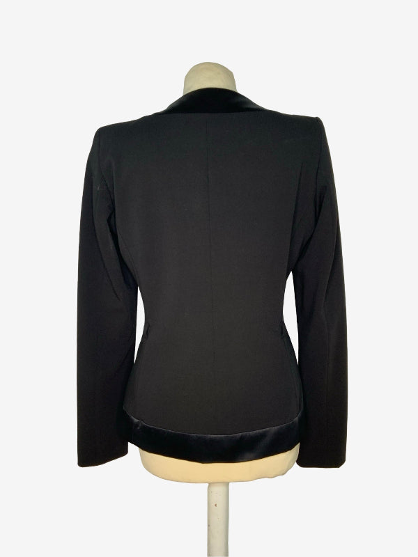 A black long-sleeve blazer jacket with contrasting black velvet trim at the collar and hem, displayed on a cream-colored mannequin torso against a light gray background.