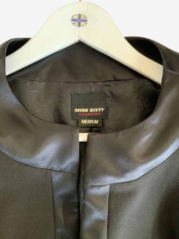 Close-up of a black  satin-like garment on a white hanger, showing the collar, front opening, and an interior size label that reads Miss Sixty Collection Medium.