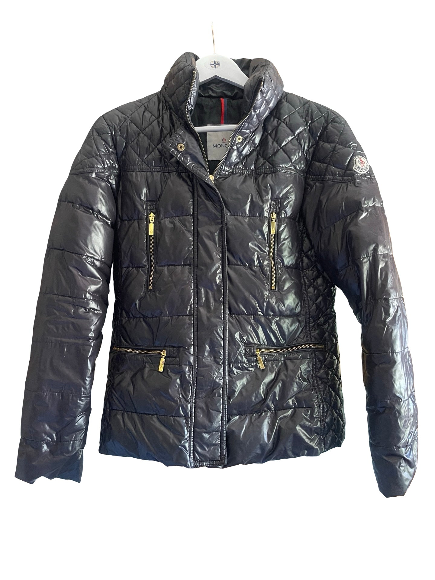 A black quilted puffer jacket with gold-tone zippers, hanging on a white hanger against a plain white background.