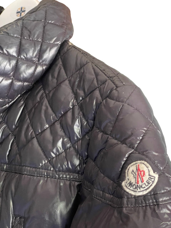 Close-up of a dark gray quilted puffer jacket with a visible circular Moncler logo patch on the sleeve, set against a plain white background.