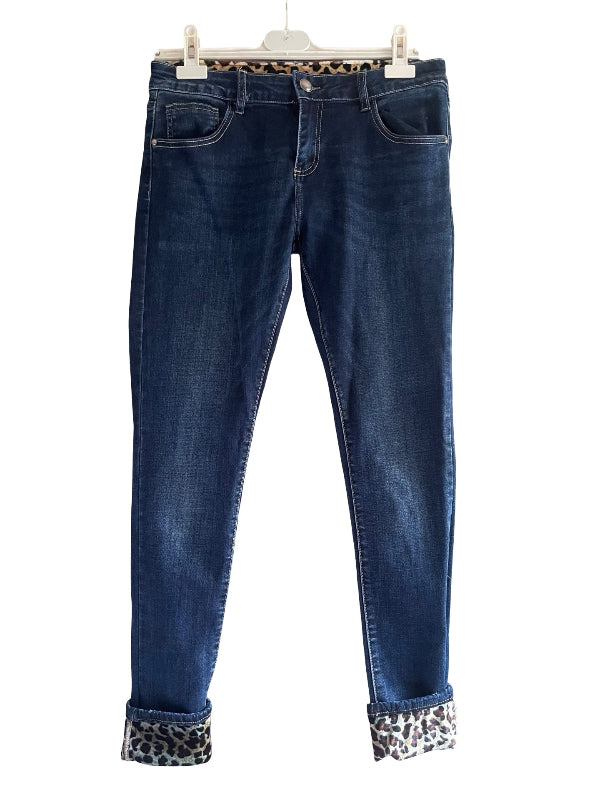 Dark blue skinny jeans with leopard print trim at the waistband and cuffs, hanging on a white plastic hanger against a white background.