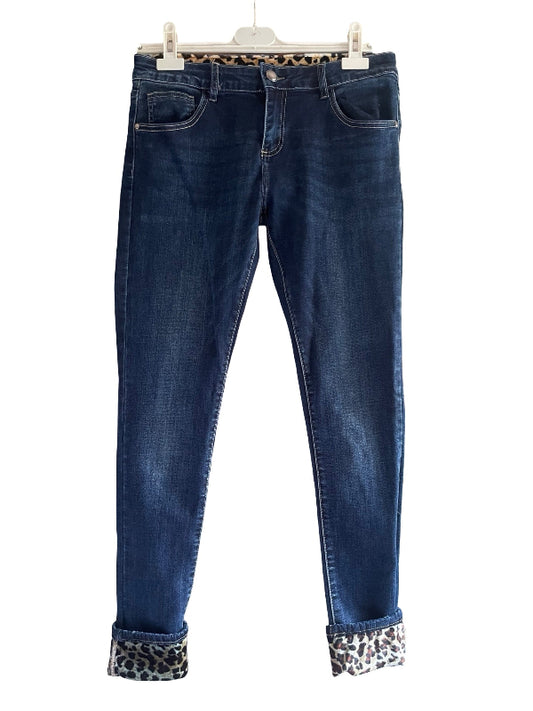 Dark blue skinny jeans with leopard print trim at the waistband and cuffs, hanging on a white plastic hanger against a white background.