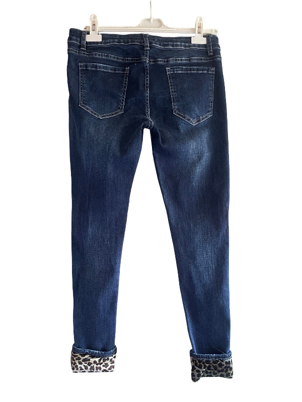 Back view of dark blue denim jeans with rolled cuffs showing a leopard print lining, hanging on a white hanger against a white background.