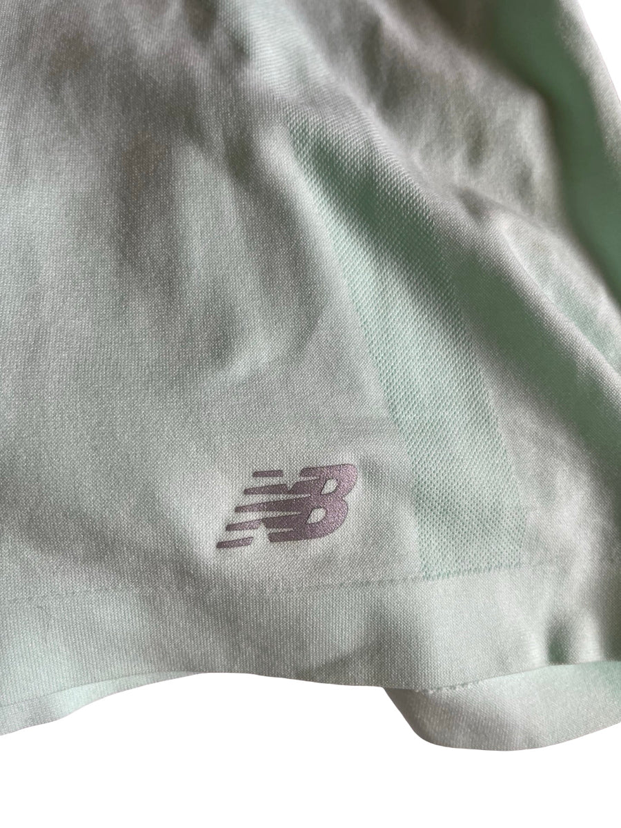 Close-up of a light sage green athletic fabric with a small embroidered New Balance 'N' logo in a muted mint green  color.