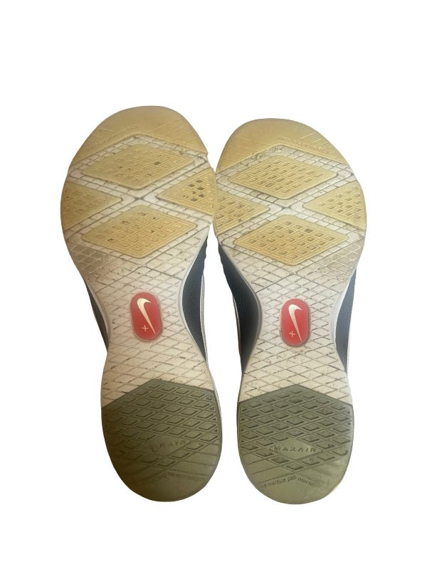 The soles of a pair of Nike sneakers, showing the textured beige and gray tread patterns and the red Nike Swoosh logo on the heel area.