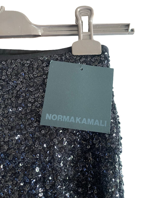 A close-up of a black sequined garment, likely a skirt, hanging from a metal hanger with a gray Normakamali brand tag attached.