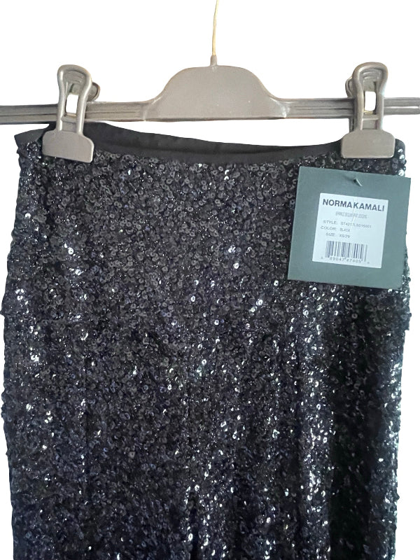 A black sequined skirt hanging from a gray plastic hanger with two metal clips, featuring a gray paper brand tag that reads NORMA KAMALI.