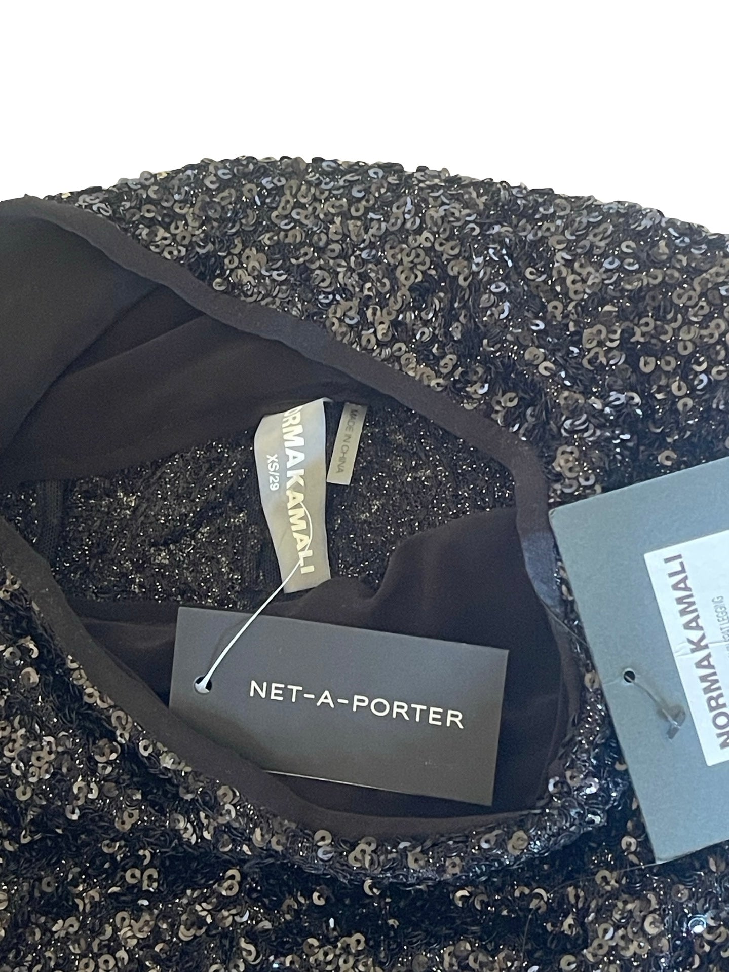 Close-up of a black sequined garment interior with visible tags including NET-A-PORTER and NORMA KAMALI.